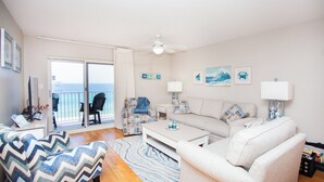 Una sala de estar con sofá, sillón, mesa de centro y vista al mar a través de un ventanal corredero.