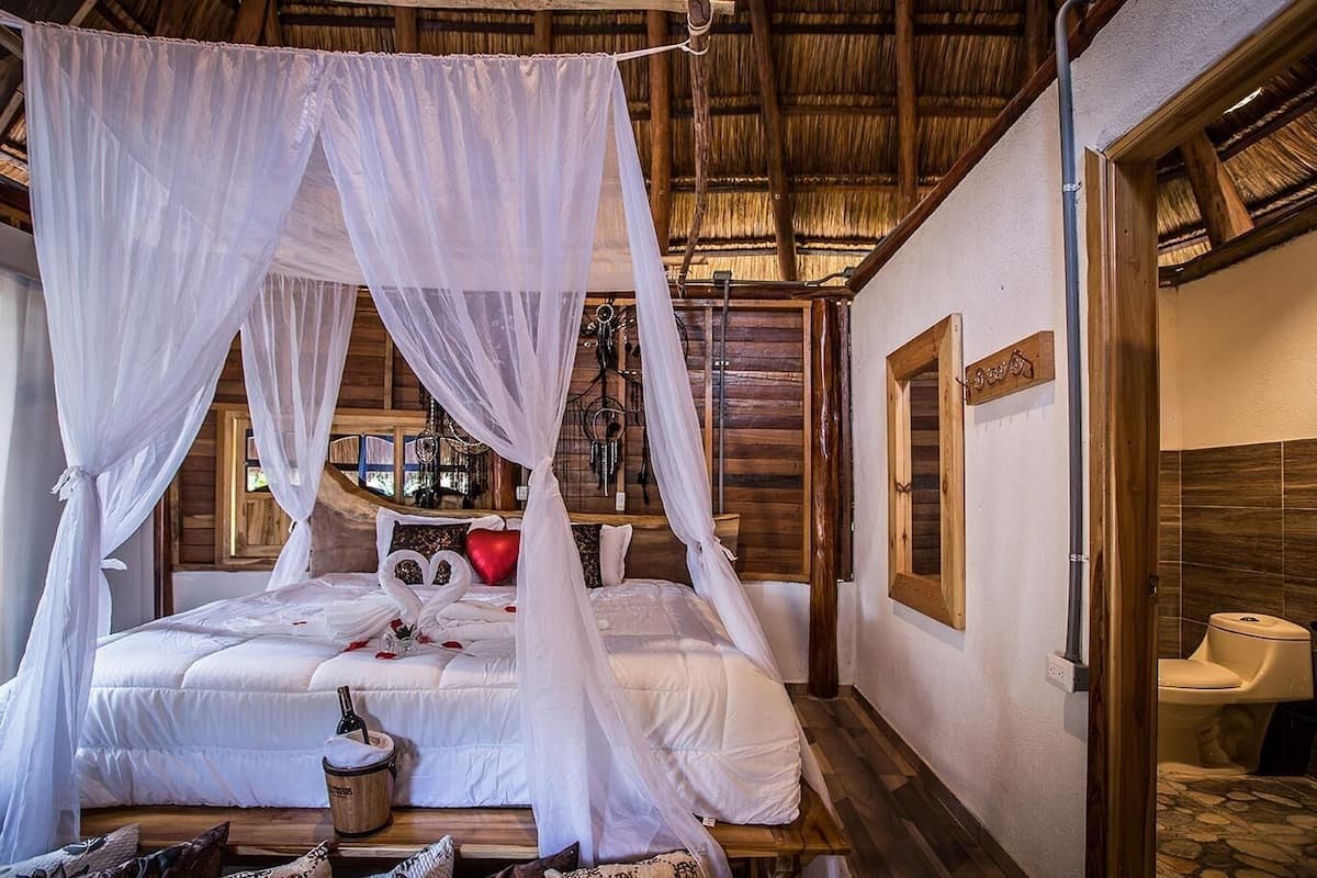 A room with a four-poster bed, a wooden floor, and a rustic wooden ceiling.