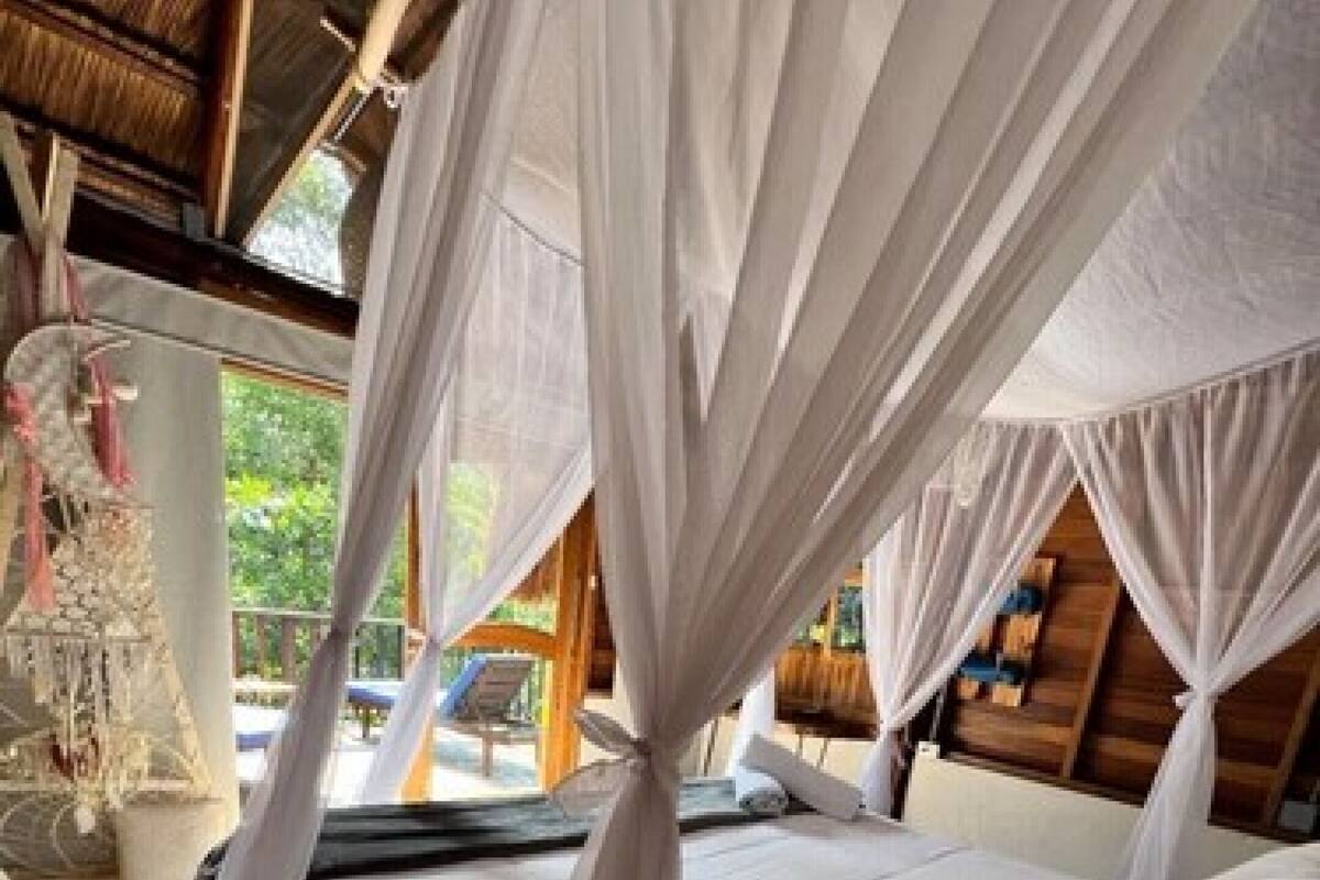 A bedroom with a canopy bed, wooden flooring, and a view of the outdoors.