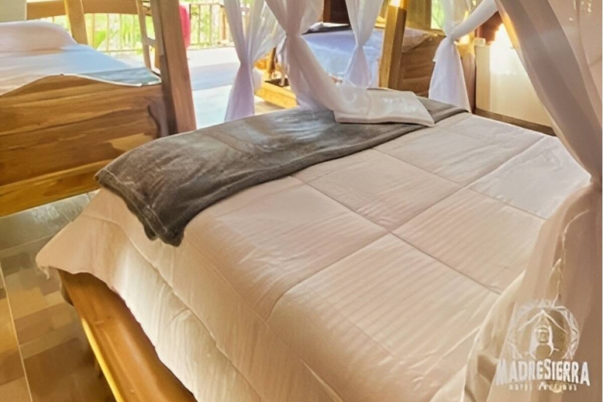 A bed with white bedding and a canopy, wooden headboard, and a bench.