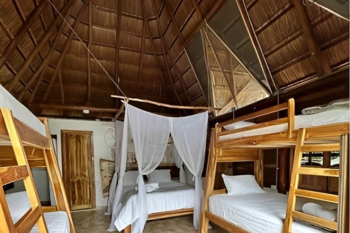 A rustic wooden room with bunk beds, a thatched roof, and a herringbone-patterned floor.