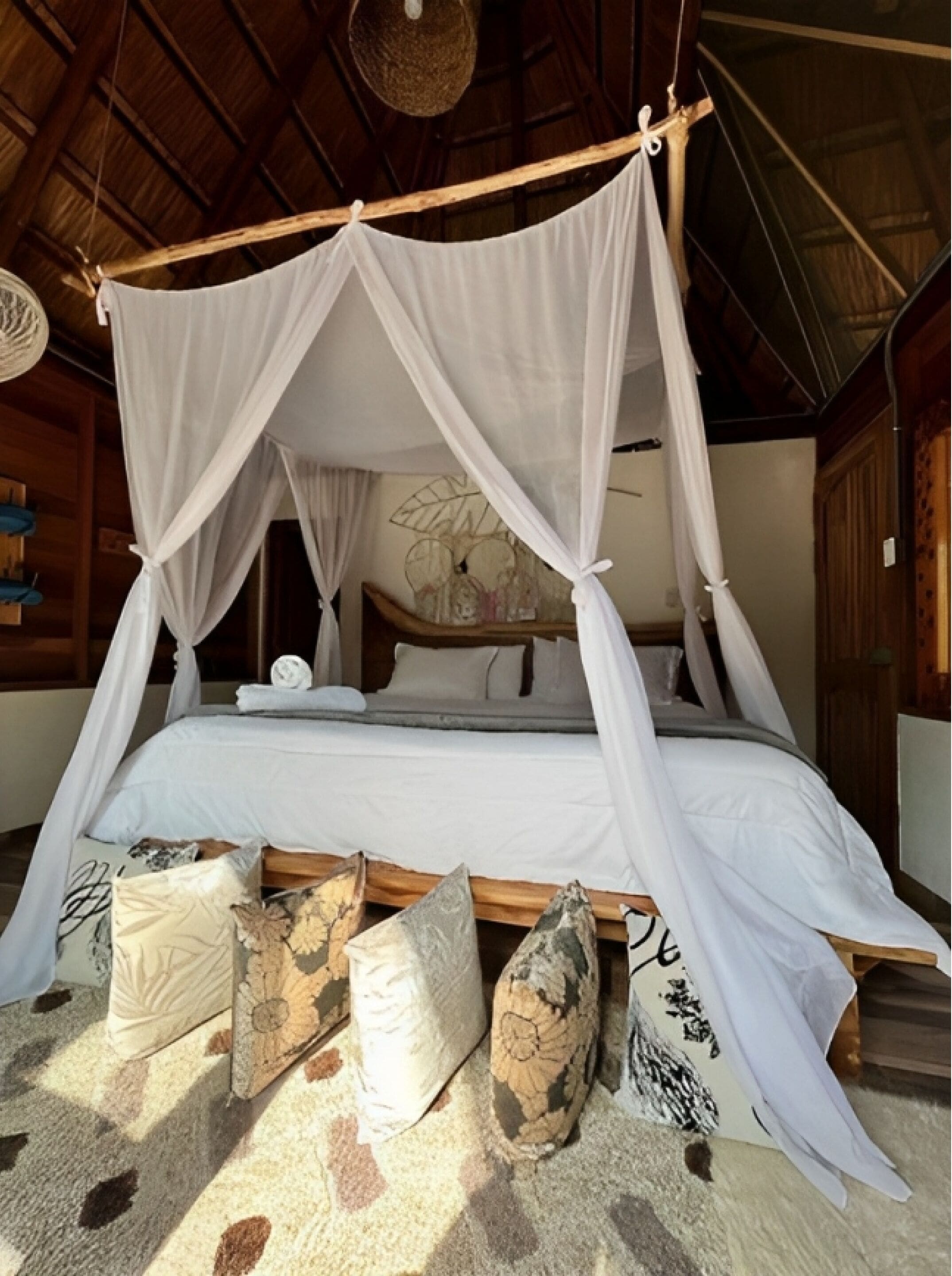 A four-poster canopy bed with white bedding, surrounded by decorative pillows and a patterned rug.