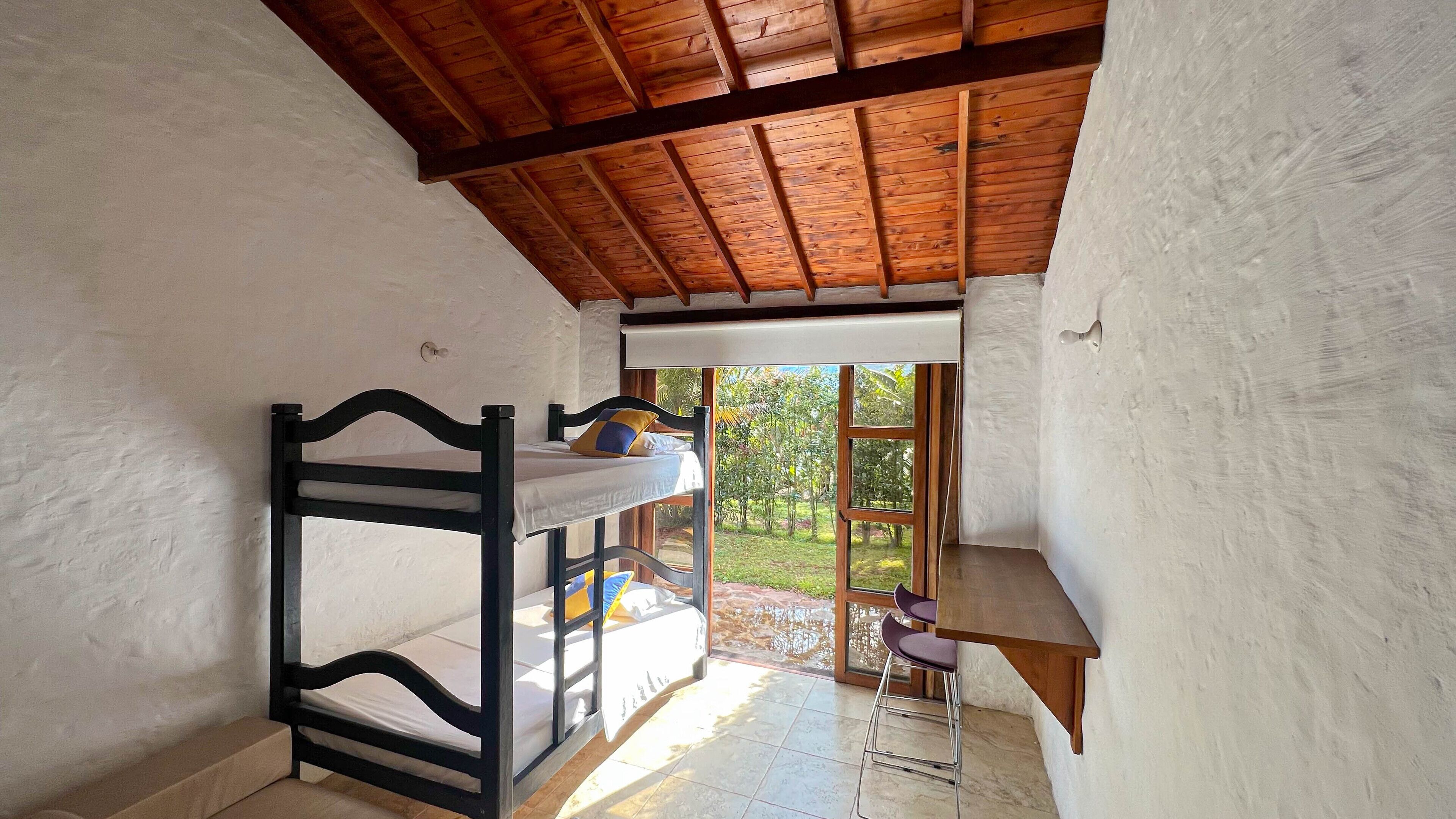 Dormitorio con literas, techo de madera, una mesita y vistas a la vegetación.