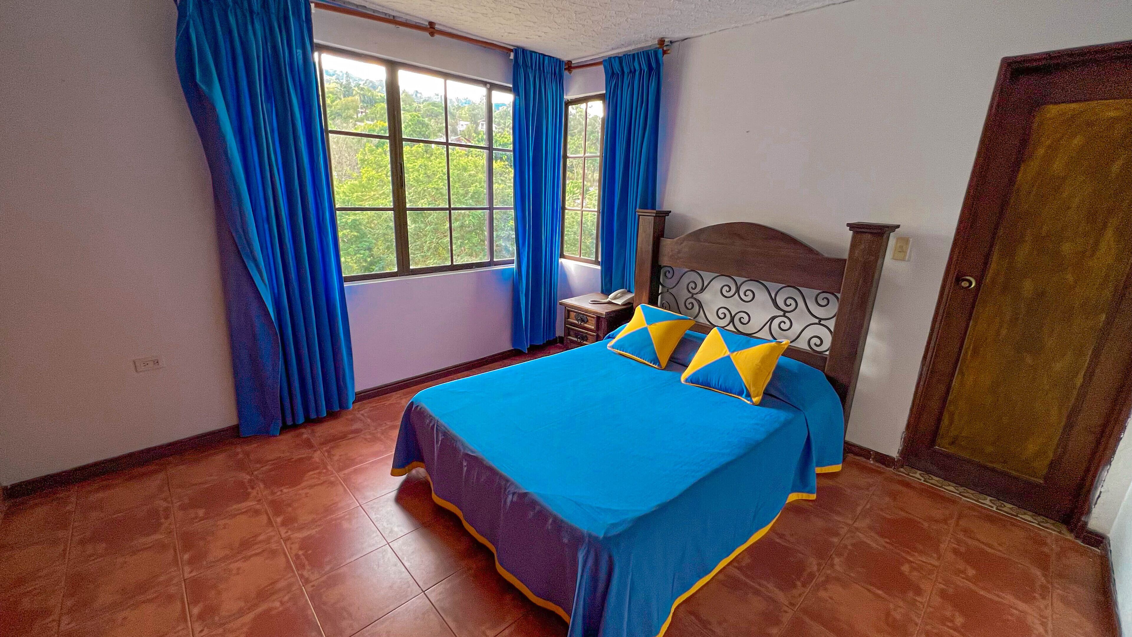 Quarto com cama, cortinas, mesa de cabeceira e porta de madeira.