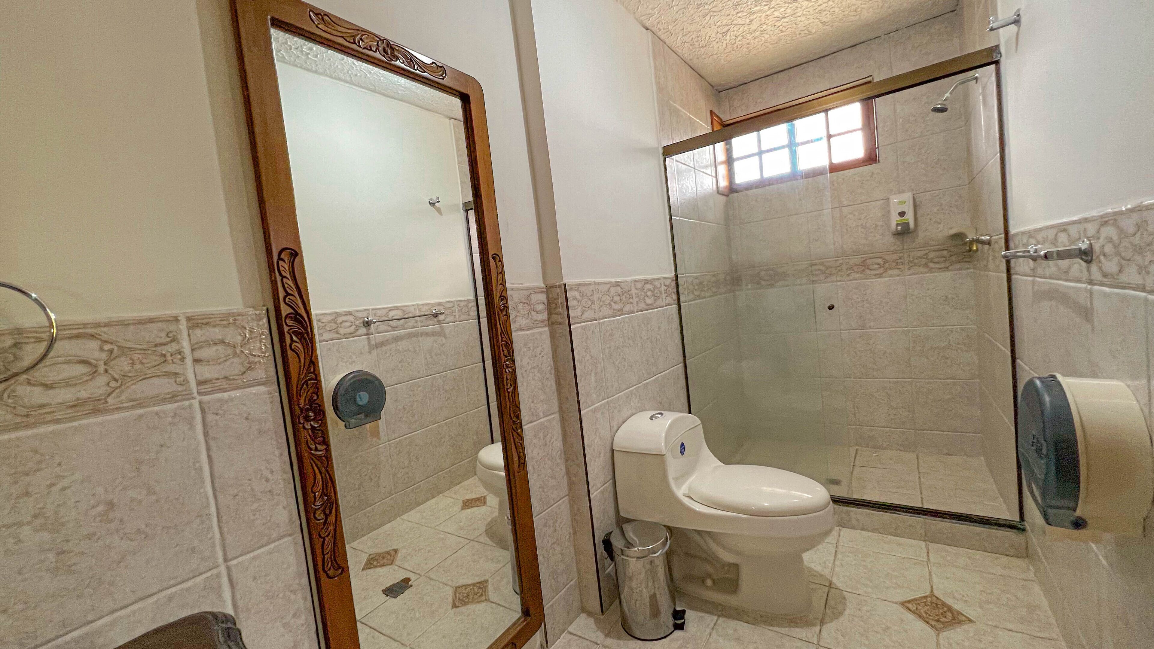 Un baño con inodoro, bidé, cubo de basura, ducha con puerta de vidrio y toallero.