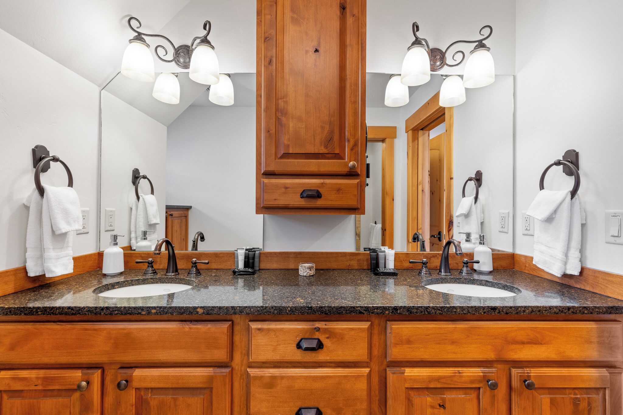 A bathroom with two sinks, wooden cabinets, a large mirror, and wall-mounted towel rings.
