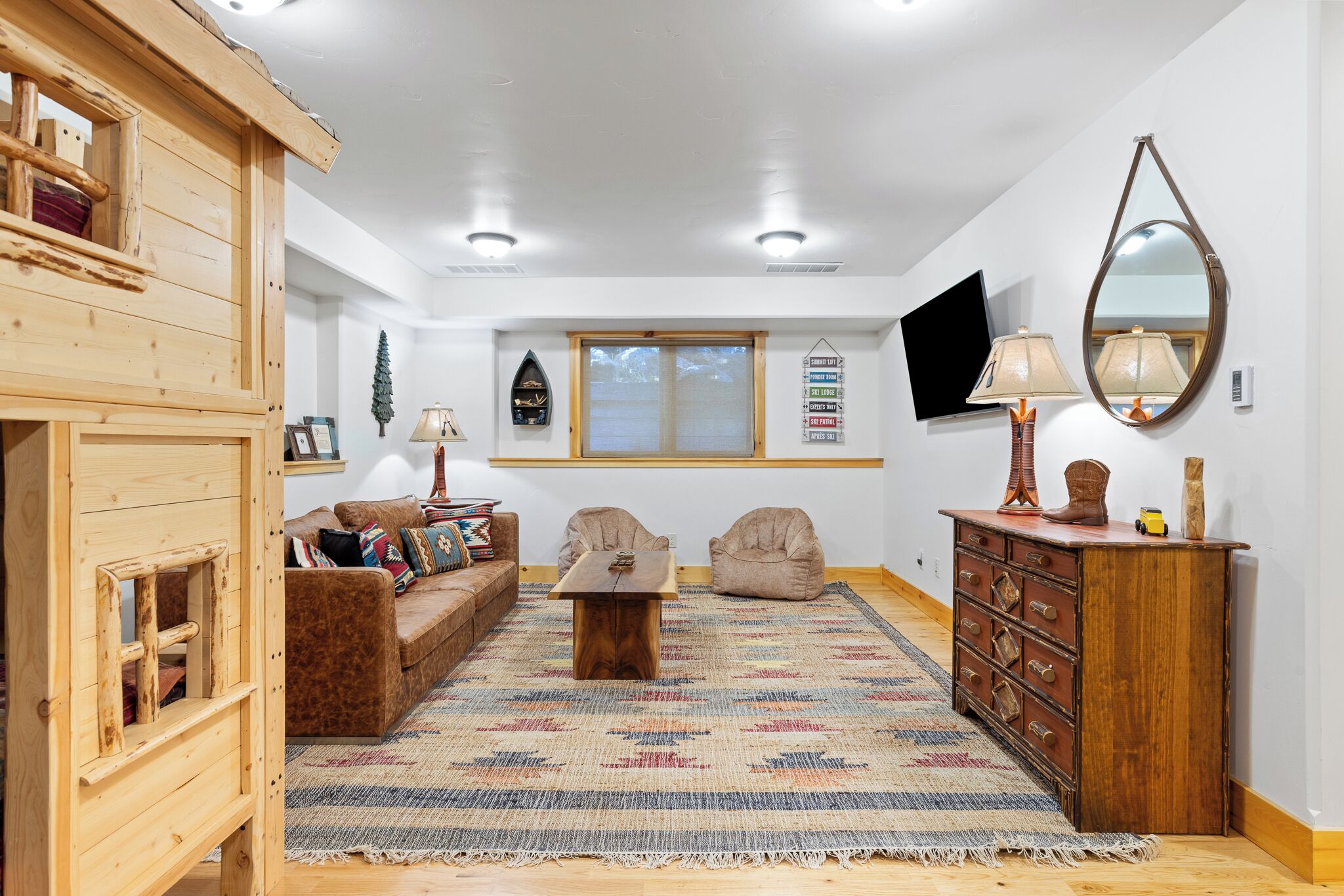 A cozy living room with a wooden playhouse, a patterned rug, a wooden coffee table, a television, and a dresser with drawers.