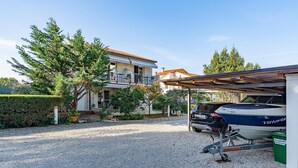 Une maison à deux étages avec un balcon, une allée en gravier et une remorque pour bateau, sur laquelle se trouve un bateau.