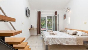 Une chambre à coucher comprenant un lit, un bureau, une chaise, un téléviseur et un balcon avec des rideaux.