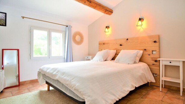 Un dormitorio con una cama grande, dos mesitas de noche, un cabecero de madera, una ventana con cortinas y dos lámparas de pared.