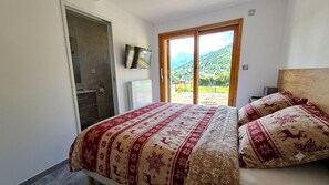 Une chambre à coucher avec un lit, une télévision, une porte-fenêtre coulissante et une vue sur un paysage montagneux.