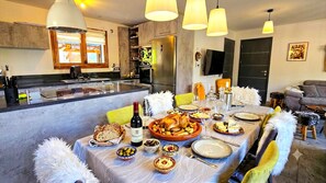 Un espace repas avec une grande table dressée pour le repas, une cuisine en arrière-plan et un coin salon avec un canapé et un téléviseur.