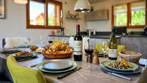 Una mesa de comedor dispuesta con platos, vasos y botellas de vino, rodeada de sillas.