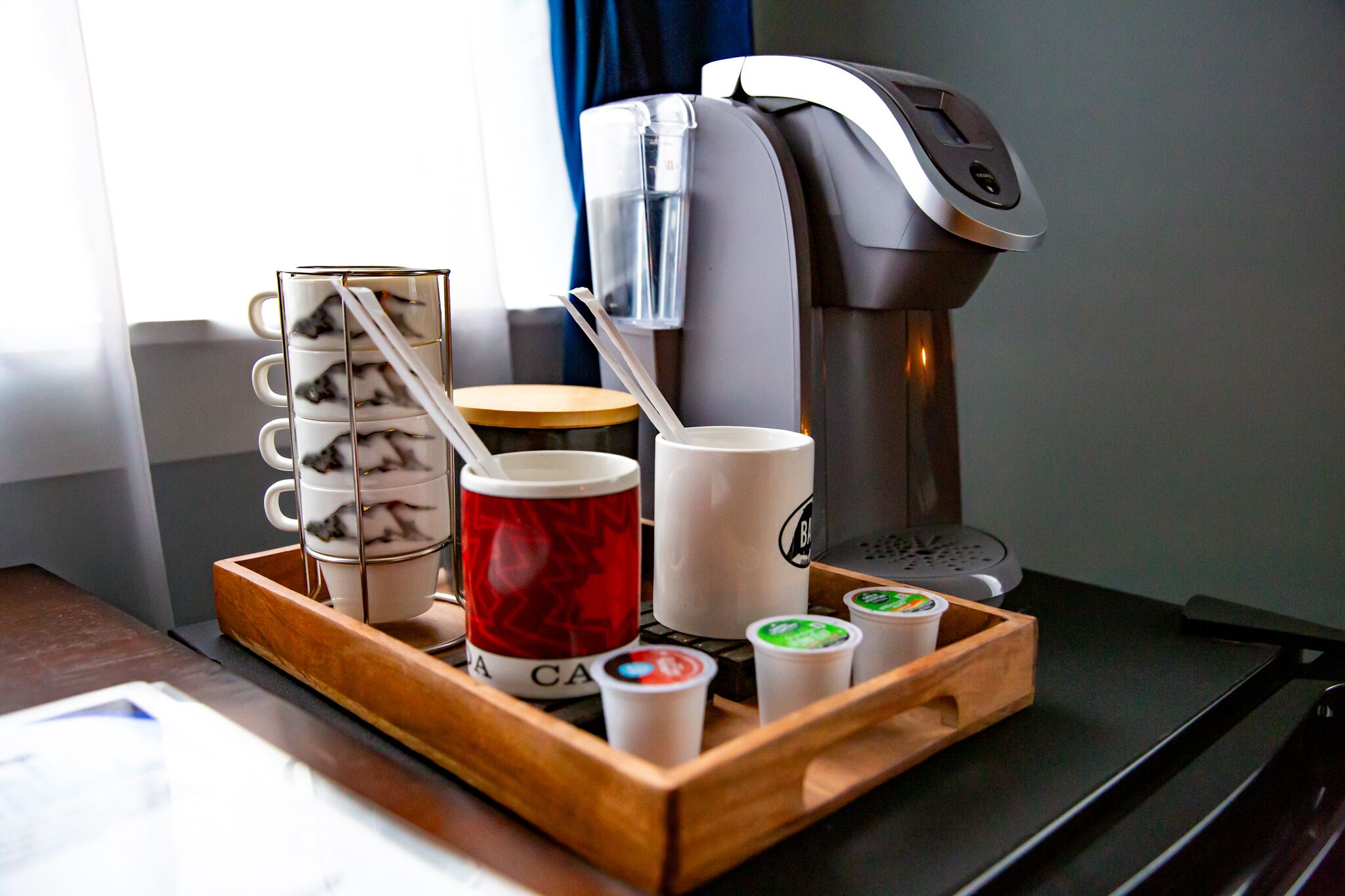 A coffee station with a coffee machine, a tray with mugs, a red mug, and two cups of coffee.