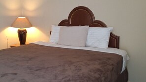 A neatly made bed with a brown blanket, a wooden headboard, and a bedside lamp. - Comanche inn (Coldwater)