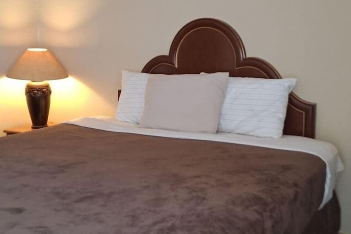 Una cama con cabecera, una lámpara y una manta.