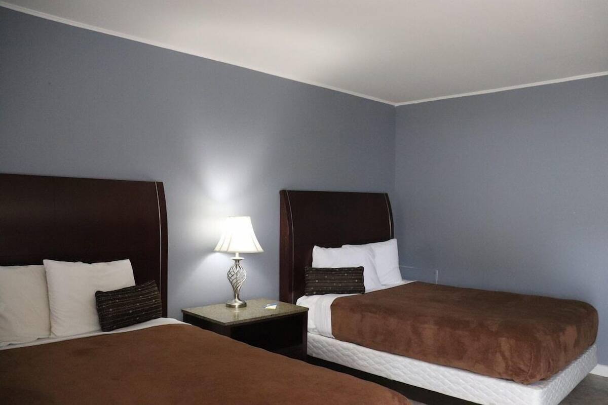 A hotel room with two beds, a nightstand with a lamp, and a blue wall.