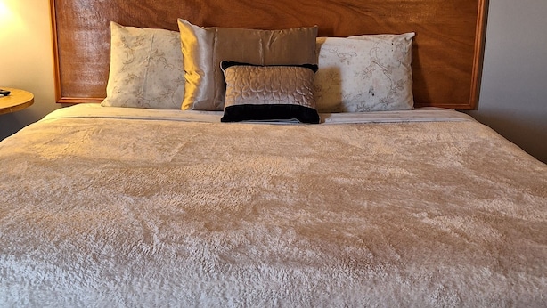 A large bed with a wooden headboard, multiple pillows, and a textured white bedspread. - Comanche inn (Coldwater)