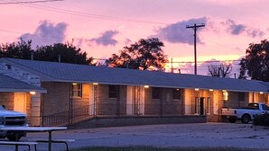A row of motel rooms with a covered parking area and a picnic table in front. - Comanche inn (Coldwater)