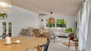 A cozy room with a wooden dining table, wicker chairs, a sofa, and a large window with a view of greenery. - Gorgeous home in Højby with WiFi (Højby)