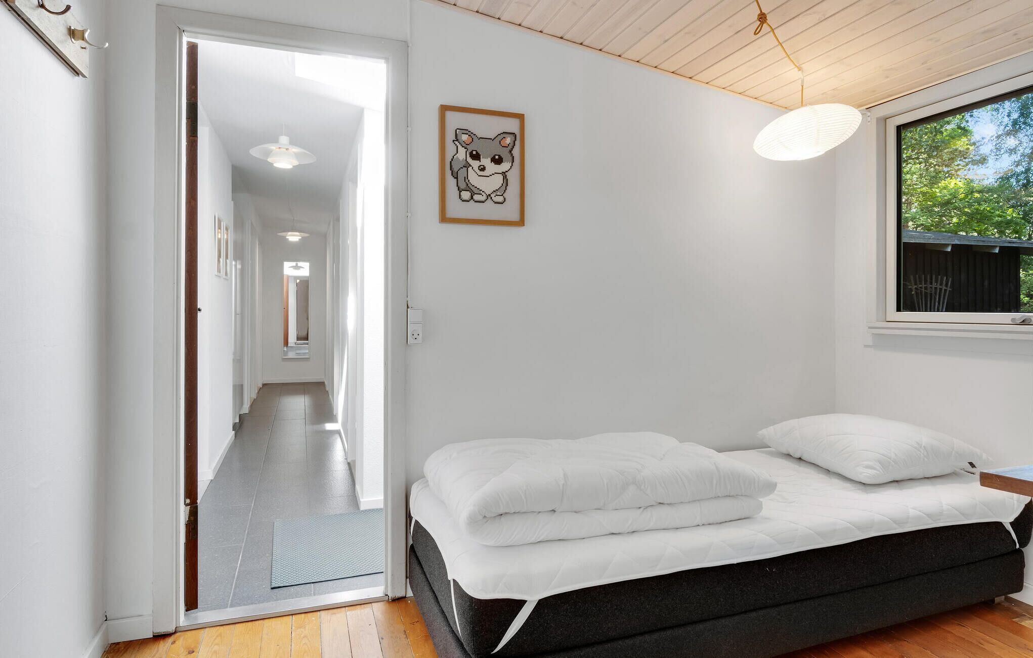 A bedroom with a bed, a window with a view of trees, a hallway, and a door leading to another room.