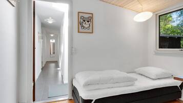 A bedroom with a bed, a window with a view of trees, a hallway, and a door leading to another room.