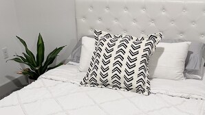Una cama bien hecha con una colcha blanca acolchada y un cojín estampado en blanco y negro.