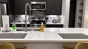 Una cocina moderna con armarios oscuros, un microondas de acero inoxidable, una estufa a gas y una cafetera.