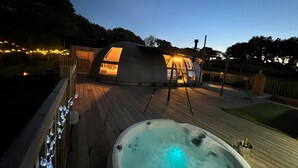 A dome-shaped structure with a hot tub in the foreground and a wooden deck. - Moonlight Tent (Tenby)