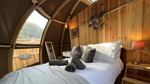 A cozy, circular room with a bed, wooden walls, a window, and a wall-mounted photo display. - Moonlight Tent (Tenby)
