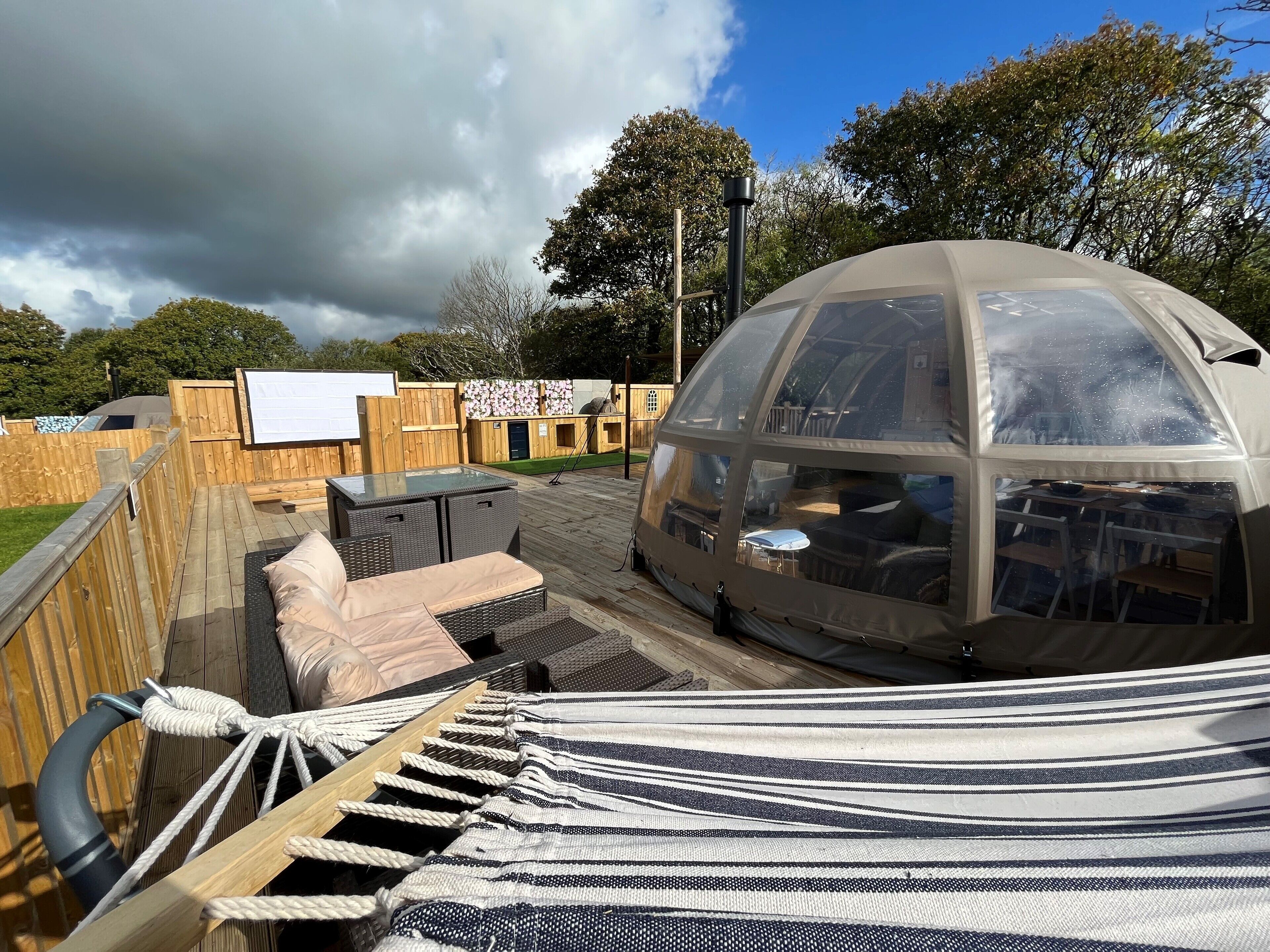 A covered outdoor seating area with a hammock, a glass-enclosed structure, and a wooden deck.