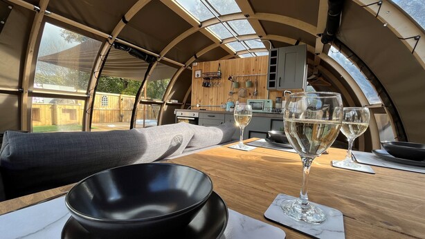 A cozy interior with a wooden table, two glasses of white wine, and a black bowl. - Moonlight Tent (Tenby)
