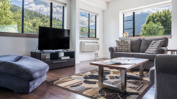 Una sala moderna con un televisor de pantalla plana, un sofá, una mesa de centro y ventanas amplias con vista a la montaña.