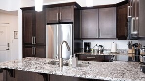 Cocina con armarios de madera oscura, refrigerador de acero inoxidable, encimeras de granito y una cafetera.
