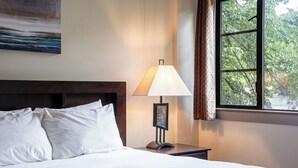 Una cama bien hecha con sábanas blancas, una lámpara de noche y un cuadro en la pared.