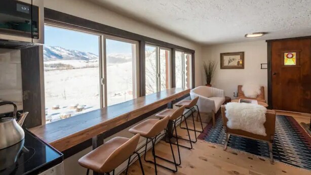 Une cuisine équipée d’une cuisinière et de chaises, située près d’une fenêtre donnant sur un paysage enneigé.