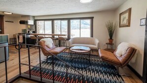Un vaste espace de vie comprenant une grande fenêtre, un canapé, un fauteuil et une table basse.