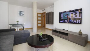 Una sala de estar moderna con un sofá gris, una mesa de centro negra redonda, un televisor montado en la pared y un mueble de madera.