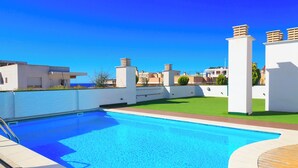 Una piscina con cubierta de madera, rodeada de paredes blancas y un cielo azul despejado.