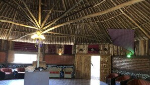 A spacious interior with a high thatched roof, wicker furniture, and a checkered floor pattern. - Explore Mara Camp (Maasai Mara)