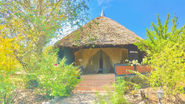 A thatched-roof structure with a covered entrance, surrounded by greenery and a stone pathway. - Explore Mara Camp (Maasai Mara)