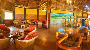 A spacious indoor area with wicker furniture and a large painting of a landscape. - Explore Mara Camp (Maasai Mara)