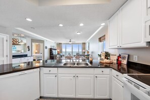 A modern kitchen with white cabinetry, a black countertop, and a central island with a sink.