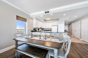 A modern kitchen with white cabinets, a central island, and a dining area with a dark wooden table and white chairs.