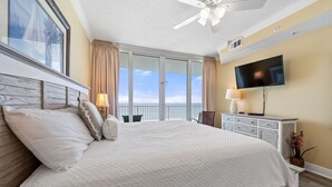 Habitación de hotel con una cama grande, ventilador de techo, televisor y balcón con vistas al cielo.