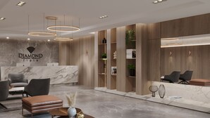 Un área de recepción moderna con un mostrador de mármol, sillas tapizadas en gris, un banco de cuero y una mesa de centro circular con objetos decorativos.