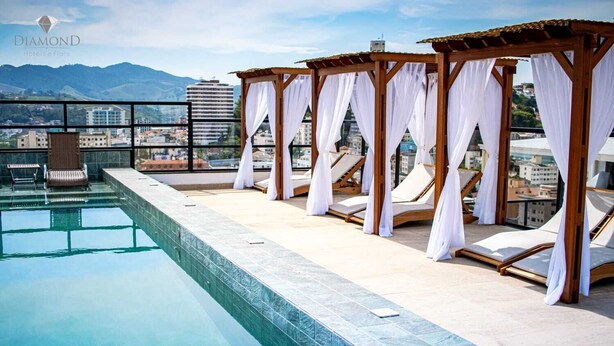 Un área de piscina en la azotea con vistas a la ciudad y las montañas, cabañas de madera y sillones de descanso.