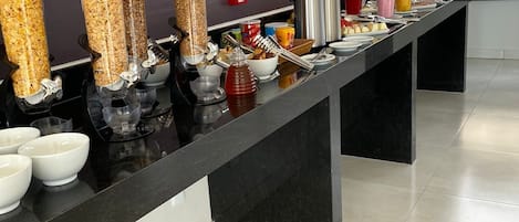 Disposição de buffet com diversos recipientes de comida e utensílios sobre uma bancada preta.