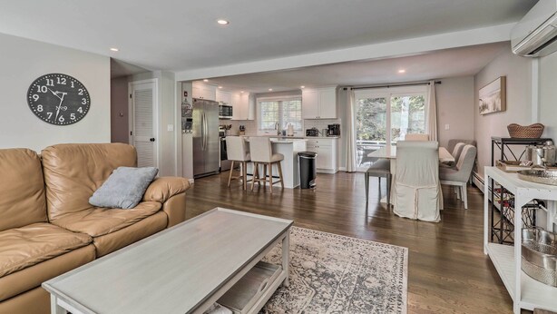 A modern living room with a leather sofa, a wooden coffee table, and a kitchen in the background. - Pool Table + Fire Pit: Wooded Hyannis Haven! (Hyannis)
