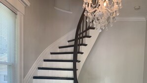 Una imponente escalera en espiral con barandillas negras y un candelabro de cristal.